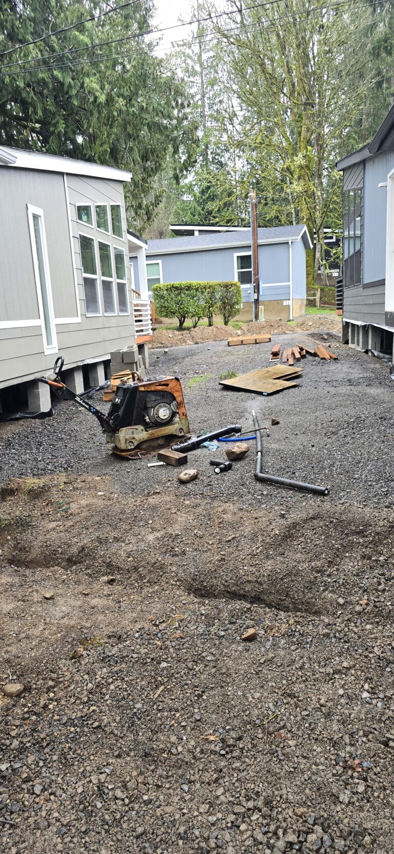 Gravel home pad being compacted for a manufactured home, with utility lines staged