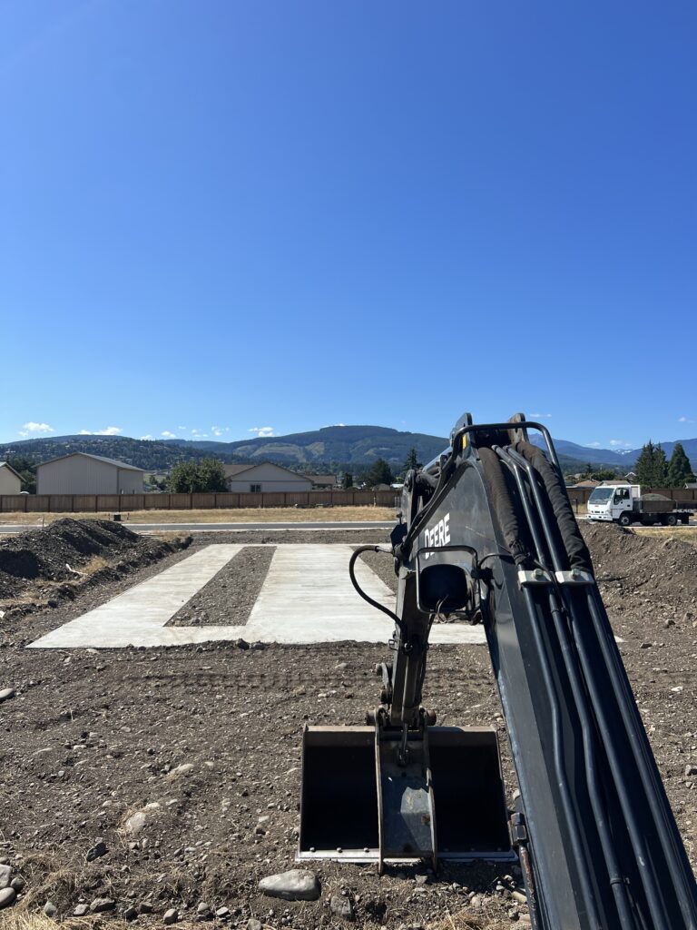 Excavator working beside a new concrete slab for a manufactured home